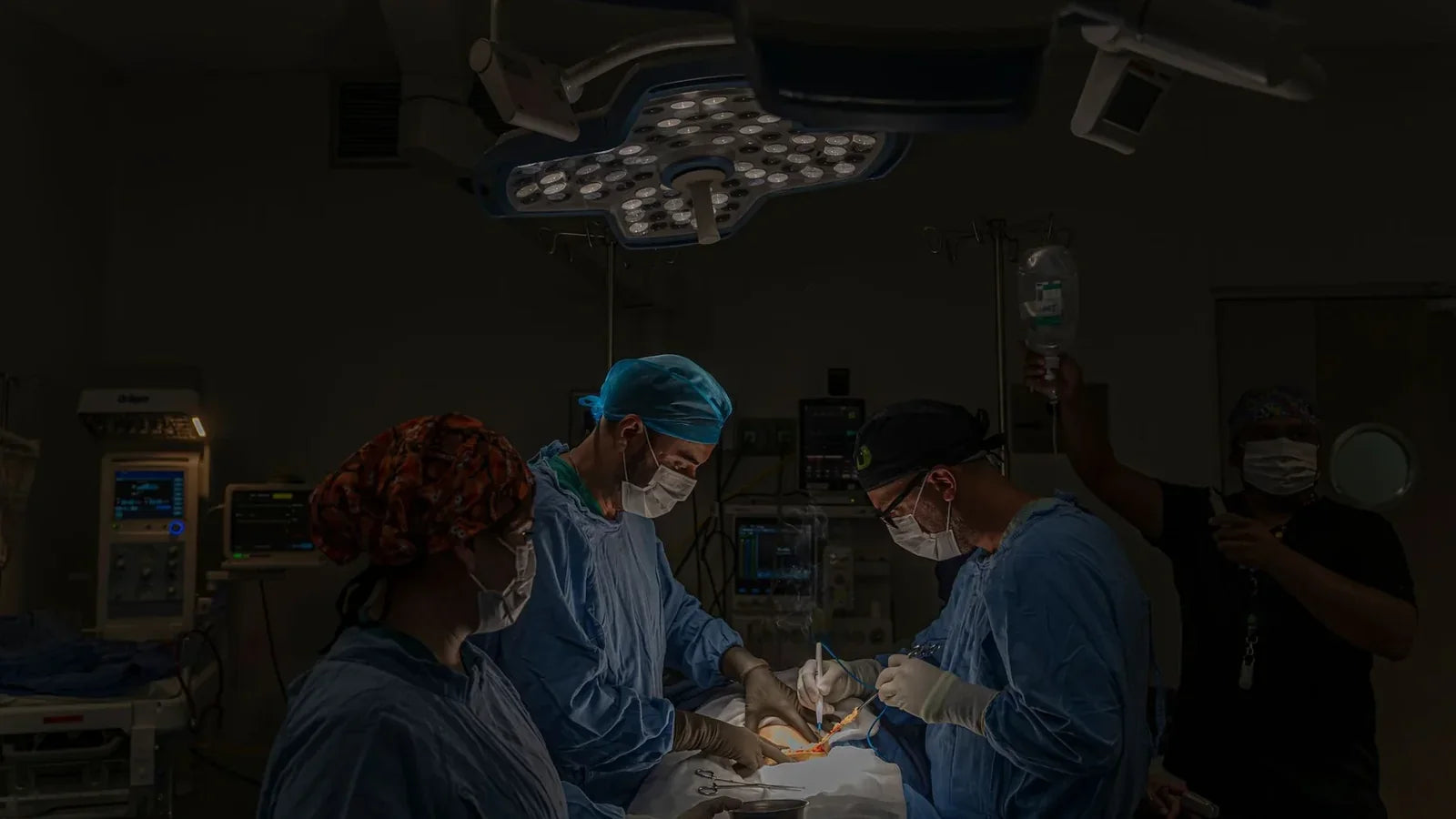 Surgical team performing a real procedure in an operating room under focused surgical lighting.