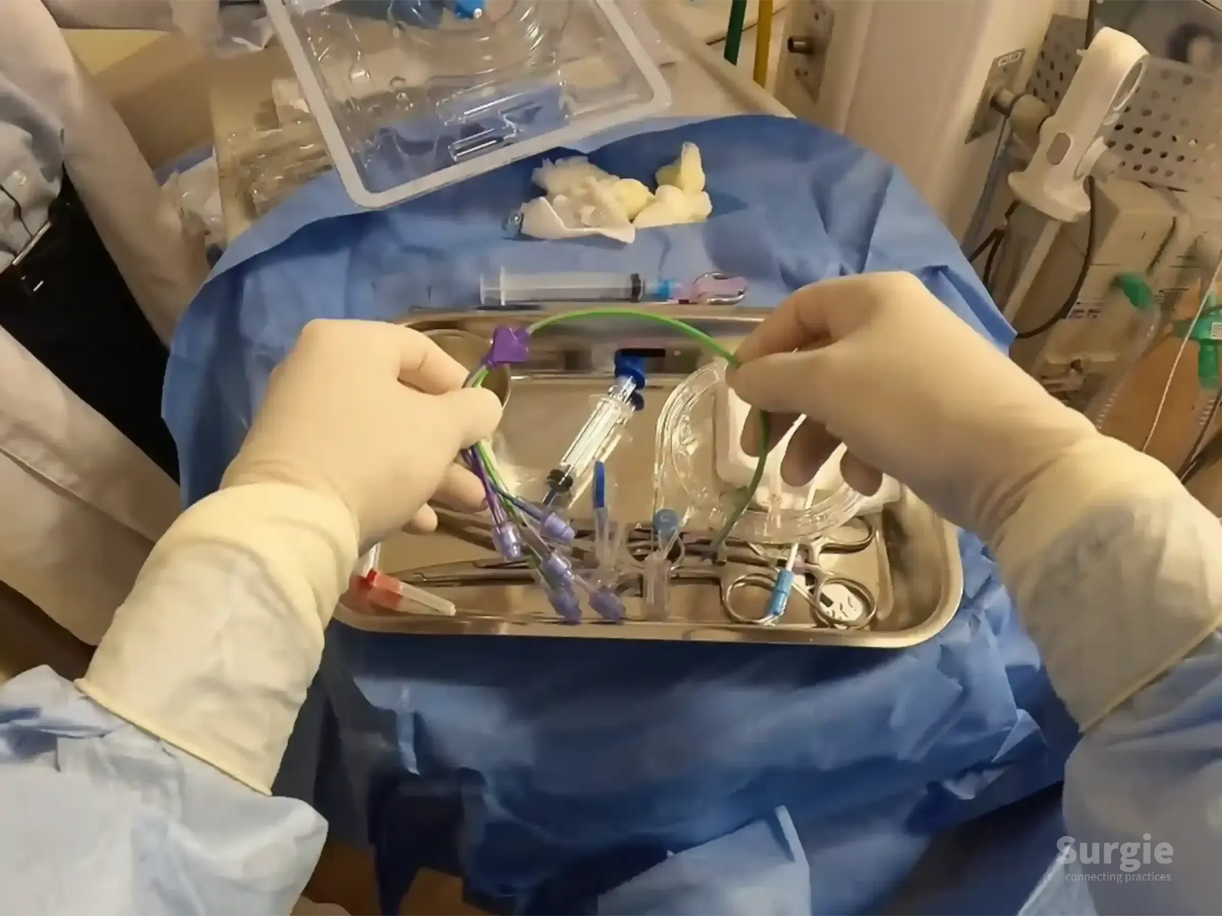 Gloved hands holding a five-lumen central venous catheter over a sterile metal tray with medical instruments.