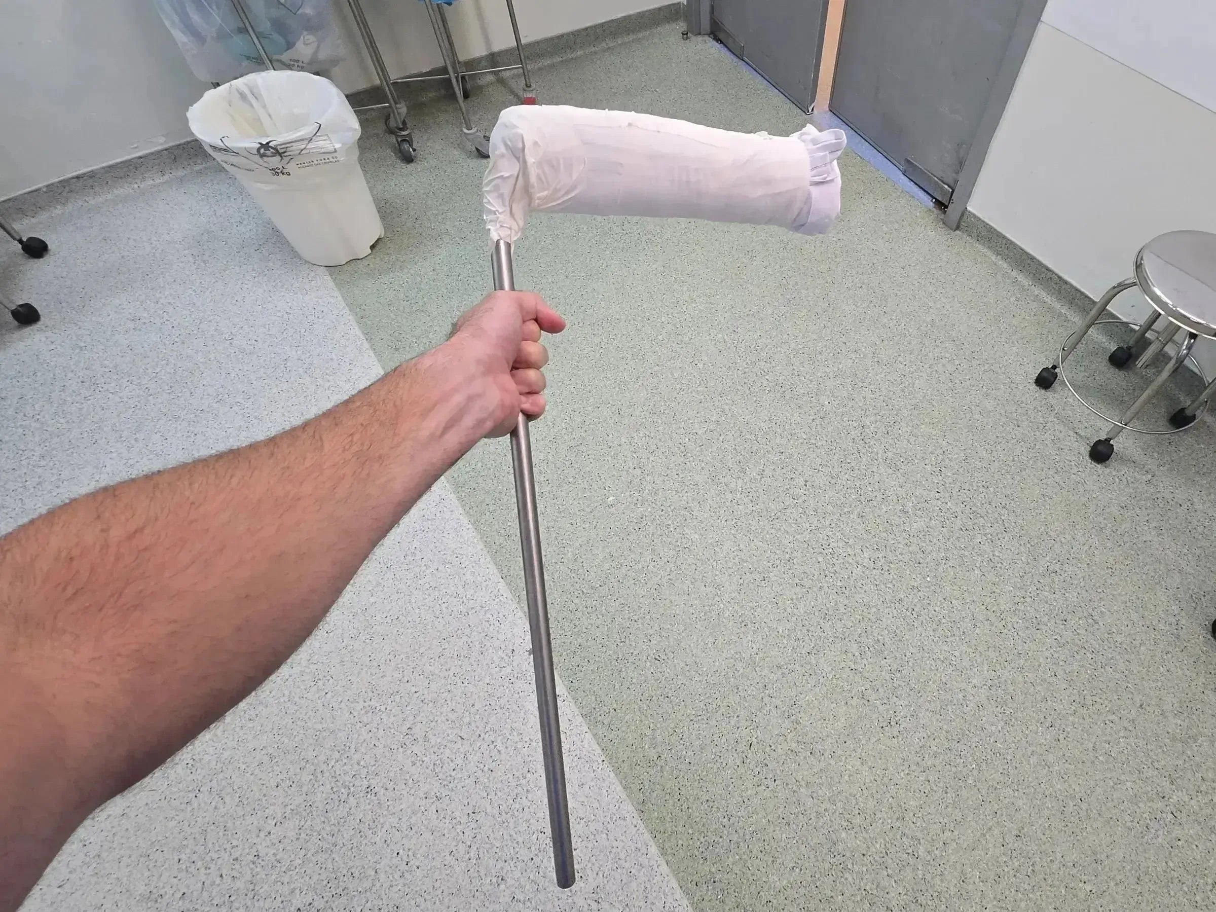 Surgeon holding a metallic intramedullary nail guide rod for infra-patellar tibial surgery in a clinical setting.
