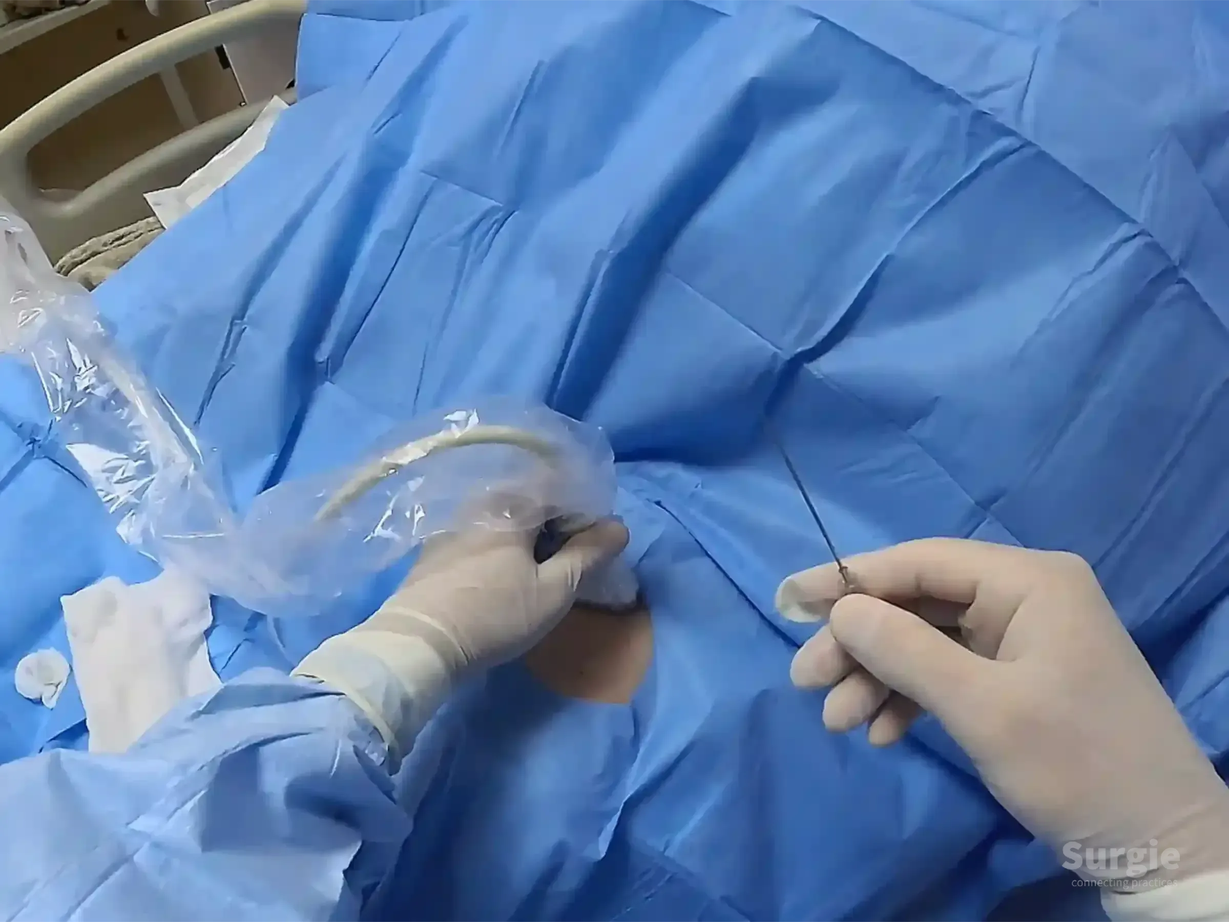 Sterile procedure using a plastic-covered ultrasound probe and needle for femoral vein catheterization on a blue drape.