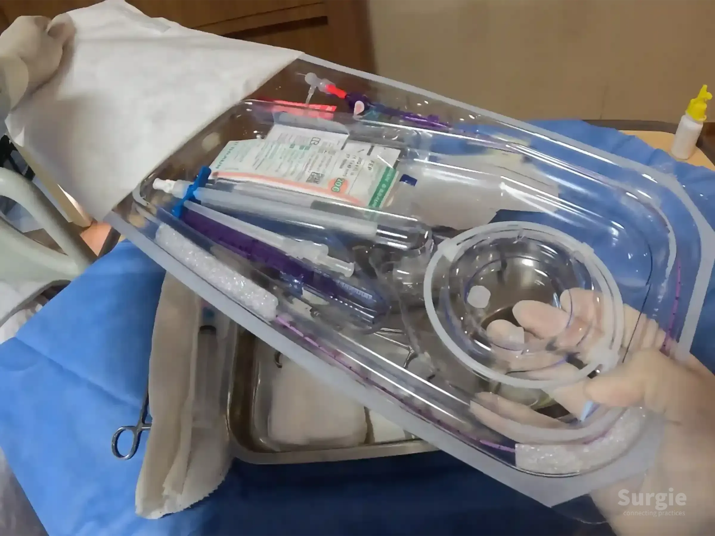 Sterile PICC placement kit in a clear plastic tray held by a gloved hand over a blue surgical drape.